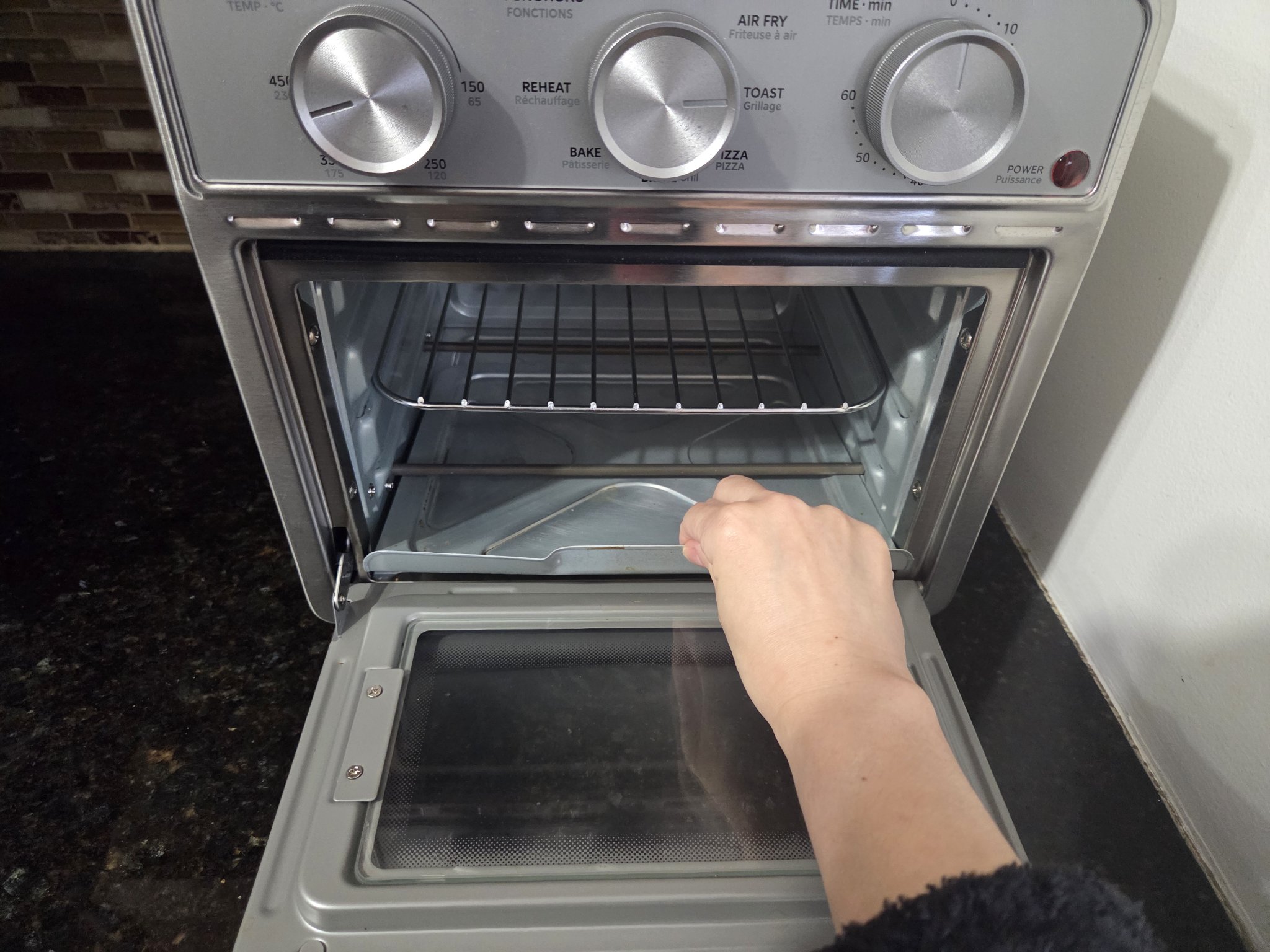 Hand pulling out the crumb tray from the bottom of the oven